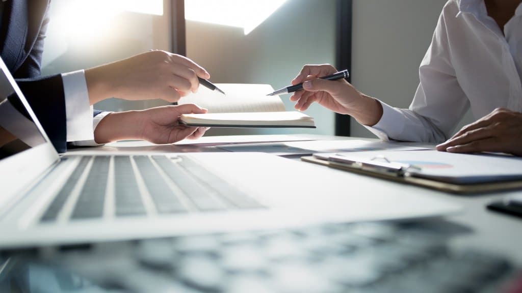 pieces of paper on a table with people holding pens